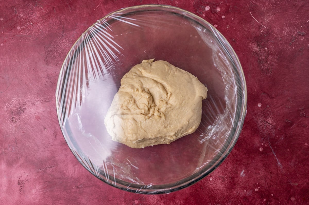 cinnamon roll dough in a bowl with plastic wrap over it