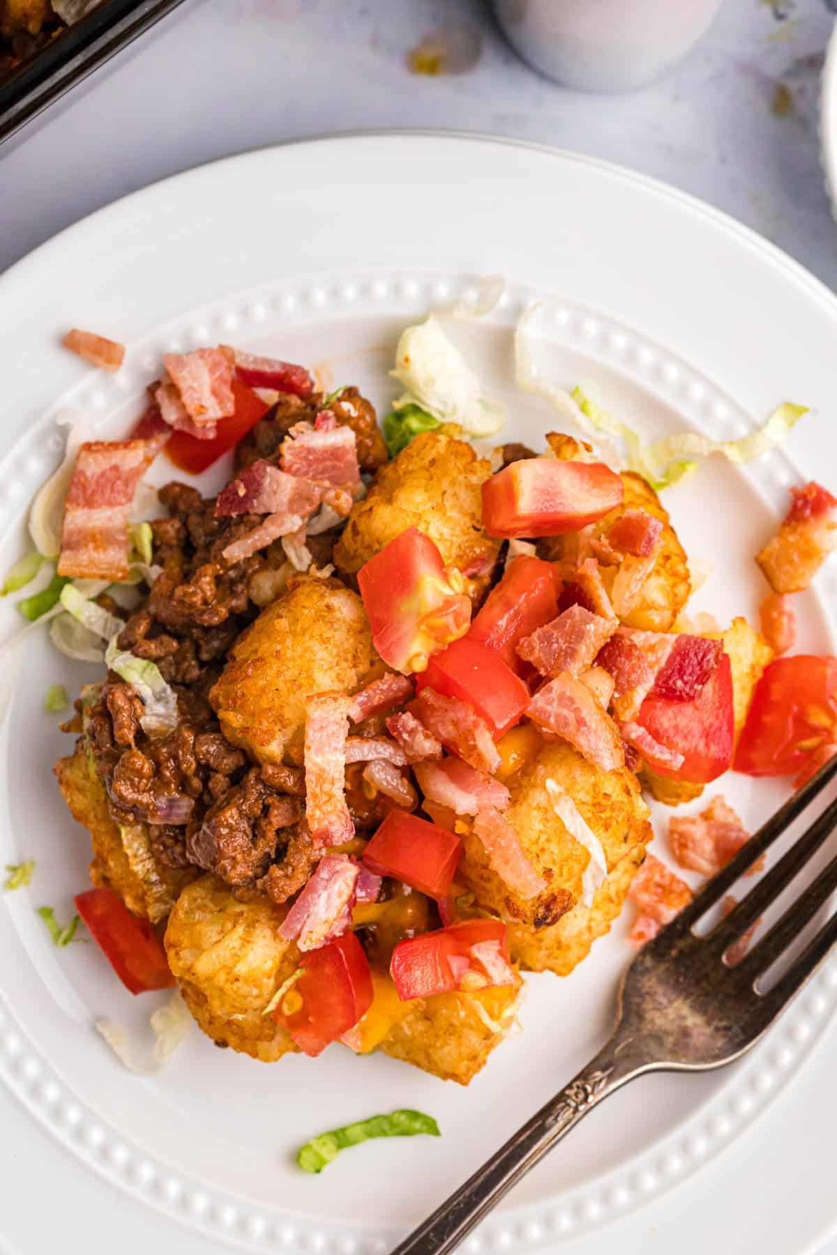 cheeseburger tater tot casserole on a plate with bacon, tomato and lettuce