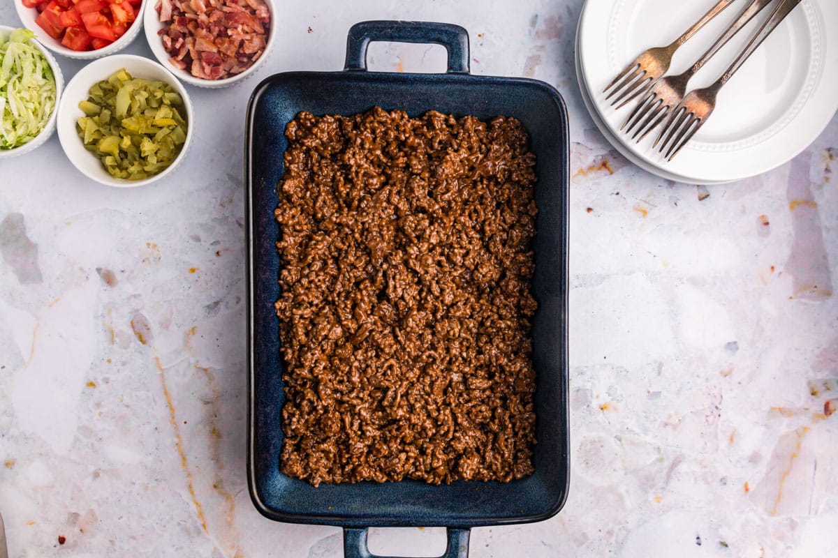 ground beef and seasonings spread in the bottom of a 9x13" baking pan
