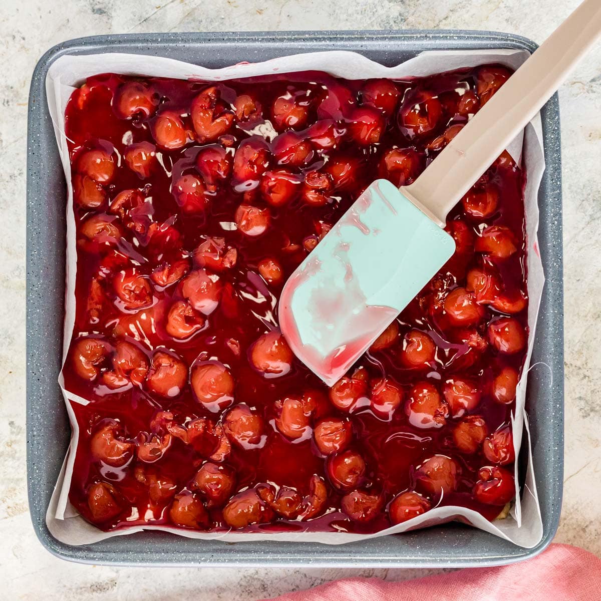 a rubber spatula spreading cherry pie filling in a pan