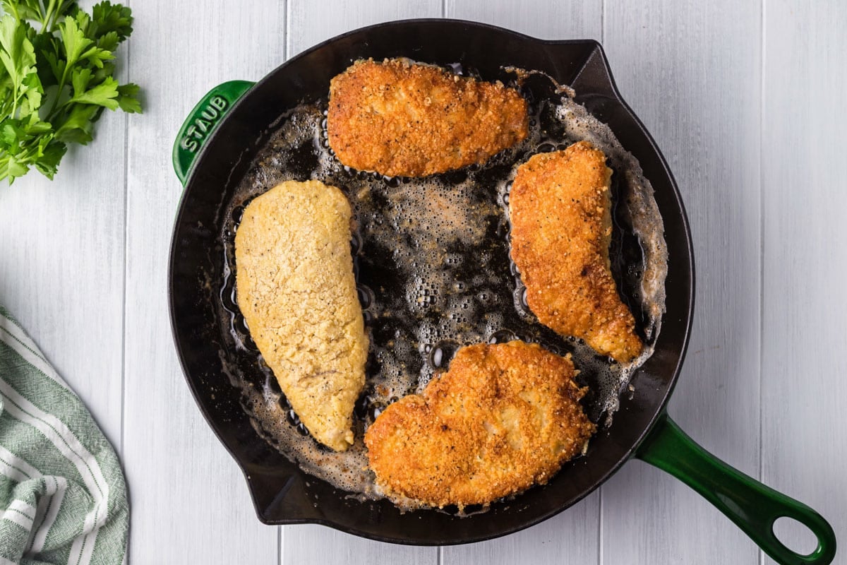 golden brown chicken frying in a cast iron skillet