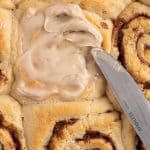 spreading cinnamon roll icing on a sweet roll