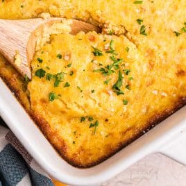 corn pudding casserole in a pan with a wooden spoon