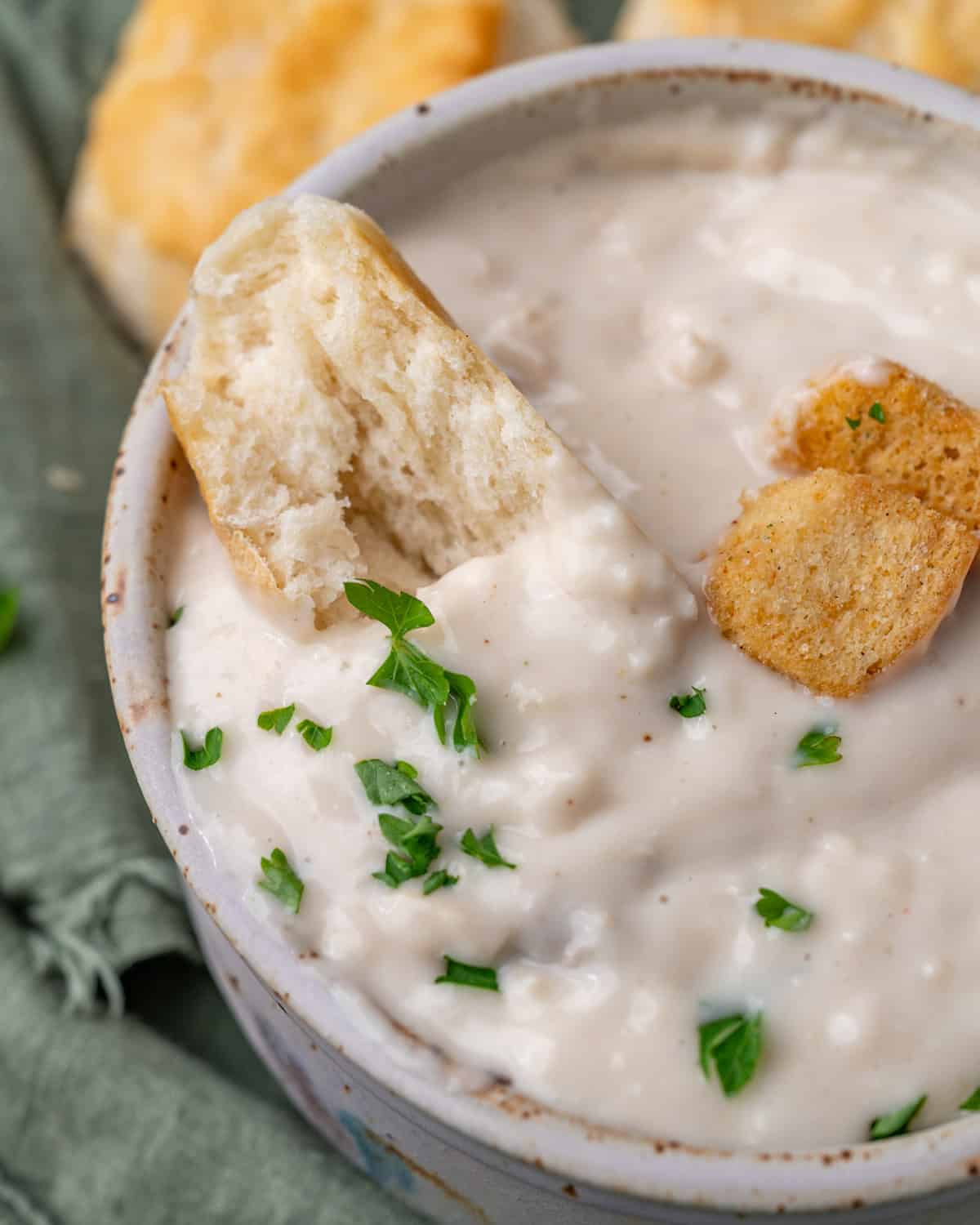 a bowl of cream of chicken soup with parsley garnish and a biscuit