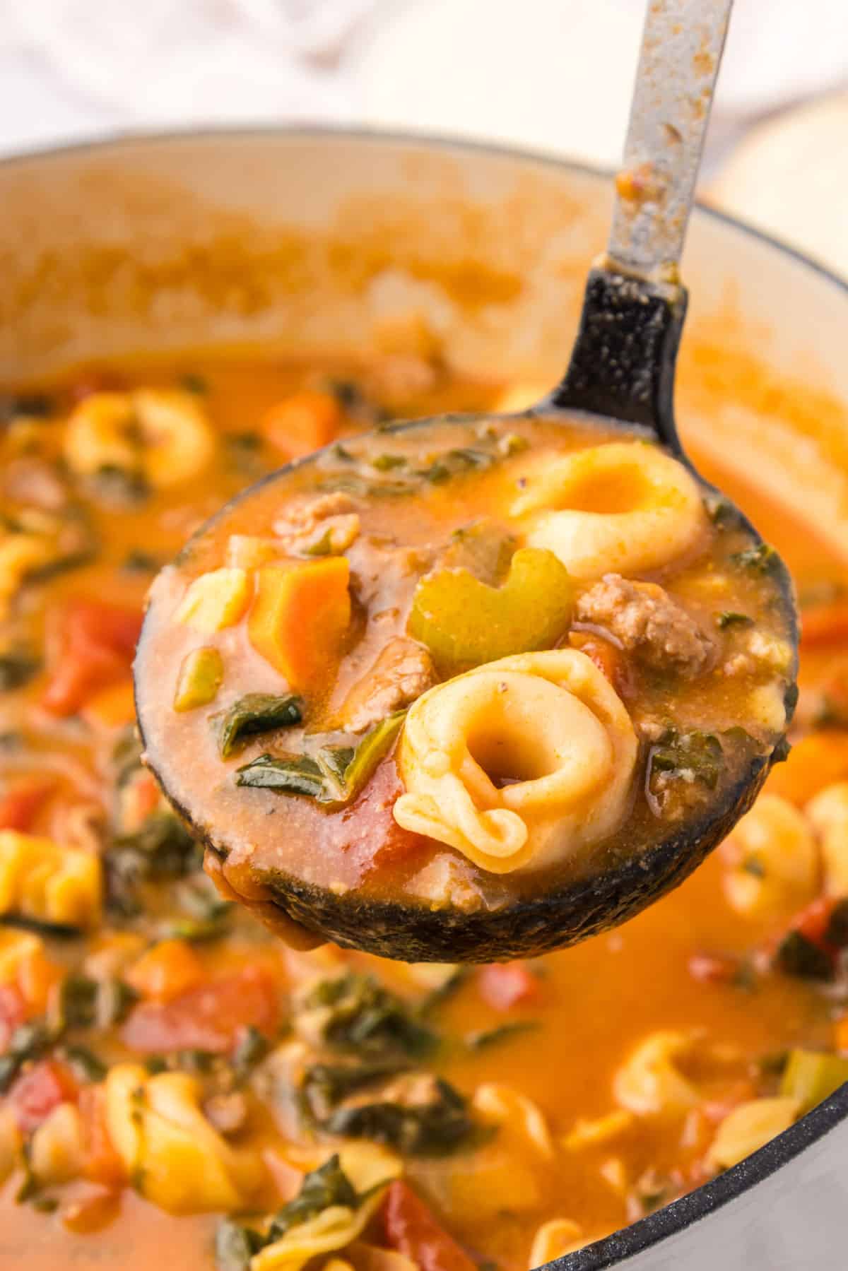 a ladle full of cheese tortellini soup with italian sausage
