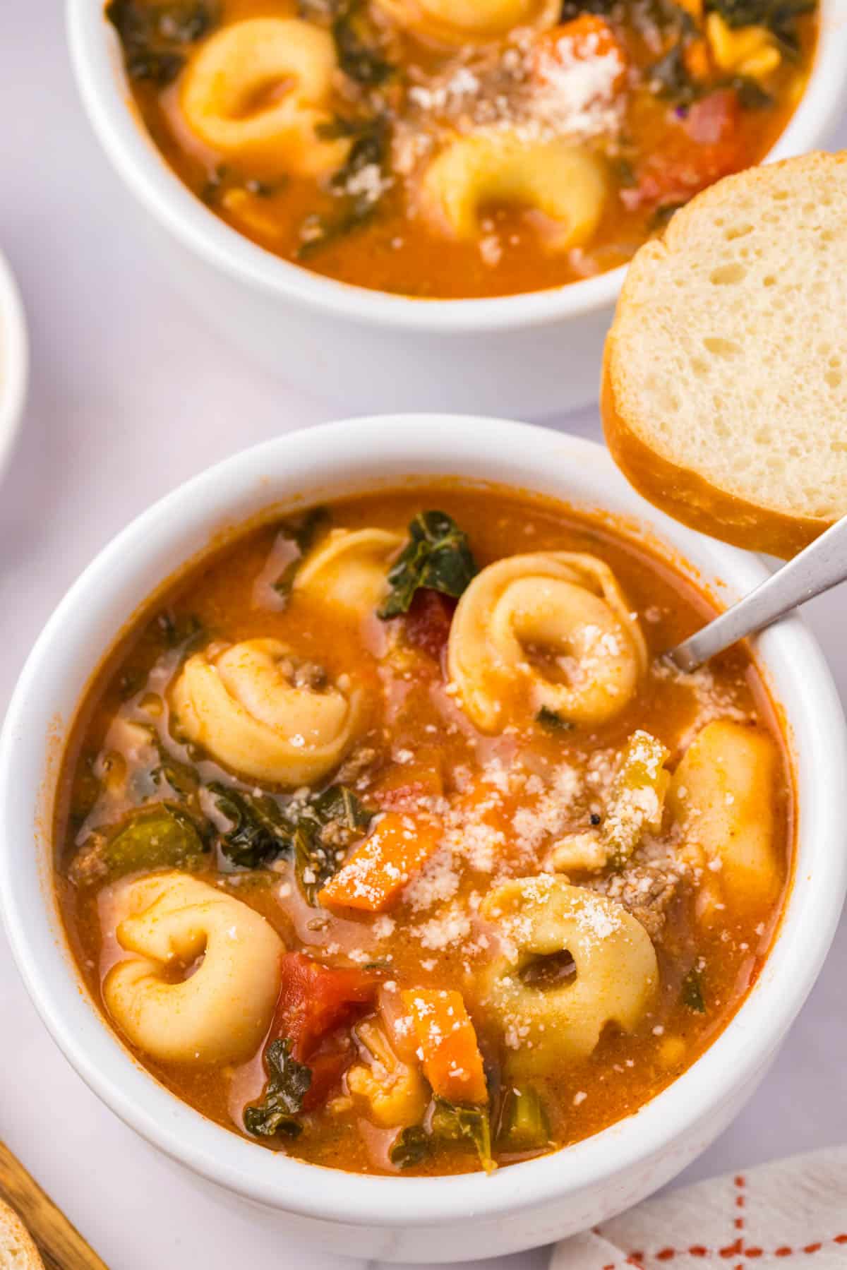 a bowl of tortellini soup with piece of bread on the side