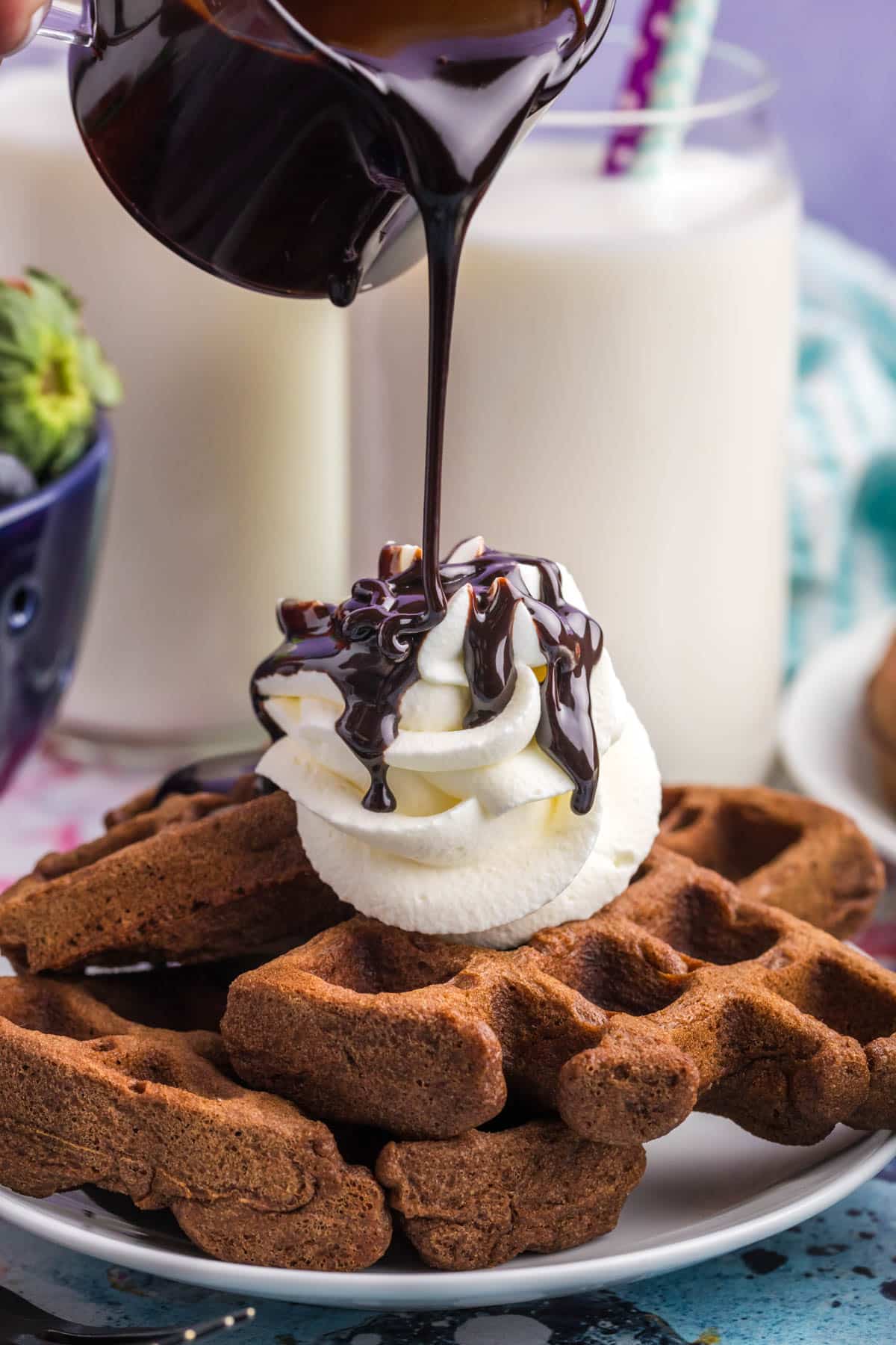 chocolate syrup pouring over chocolate waffles with whipped cream