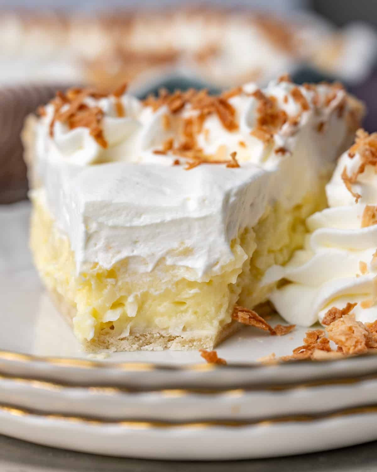 a piece of coconut cream pie on a plate with one bite out