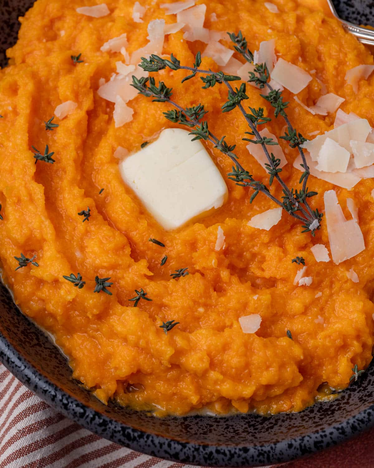 overhead view of mashed butternut squash in a bowl with fresh thyme, butter and parmesan