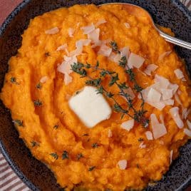 overhead view of mashed butternut squash in a bowl with fresh thyme, butter and parmesan