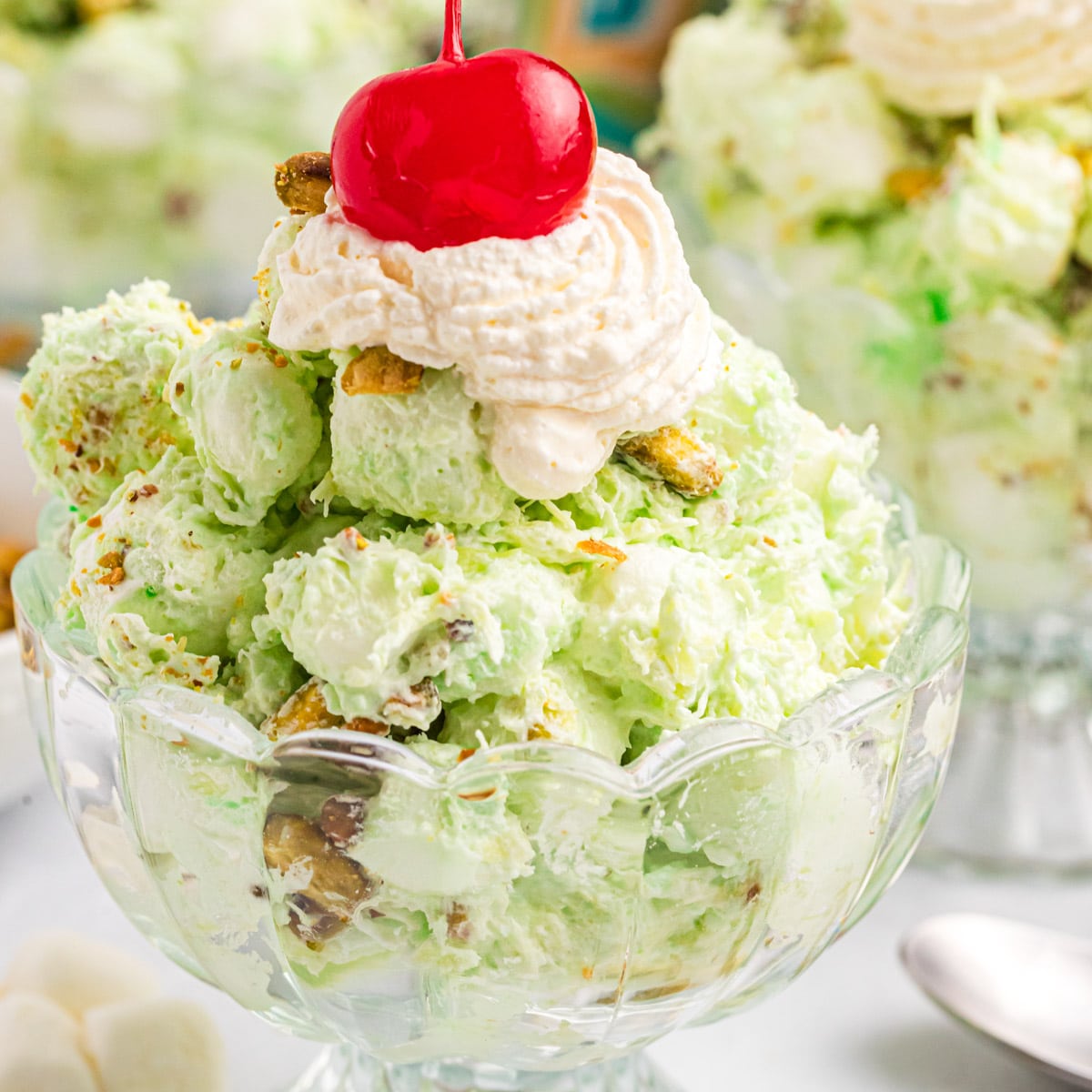 a small bowl of pistachio salad with a dollop of whipped cream and cherry on top