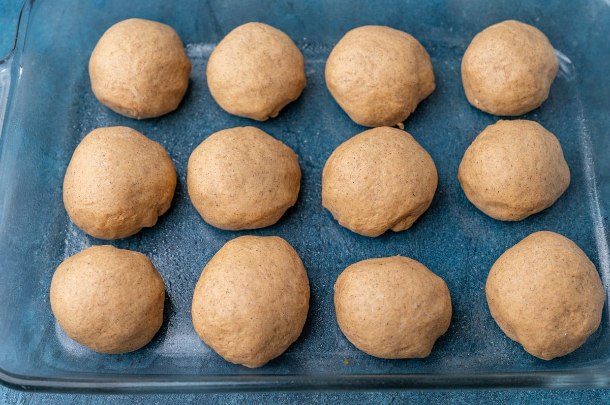 pumpkin dinner rolls in a glass pan ready to rise