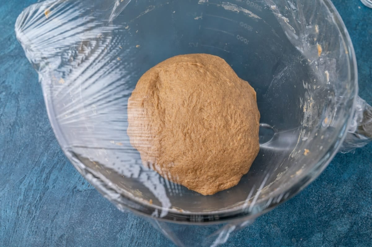 pumpkin bread dough in a glass bowl with plastic wrap over the top