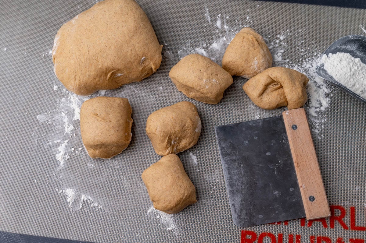 pumpkin yeast dough on a pastry mat with a dough cutter to cut rolls