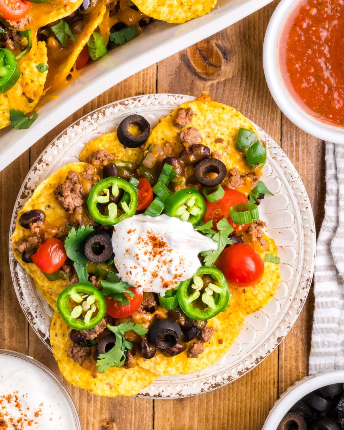 a plate of beef nachos with jalapeños, tomatoes, olives and sour cream