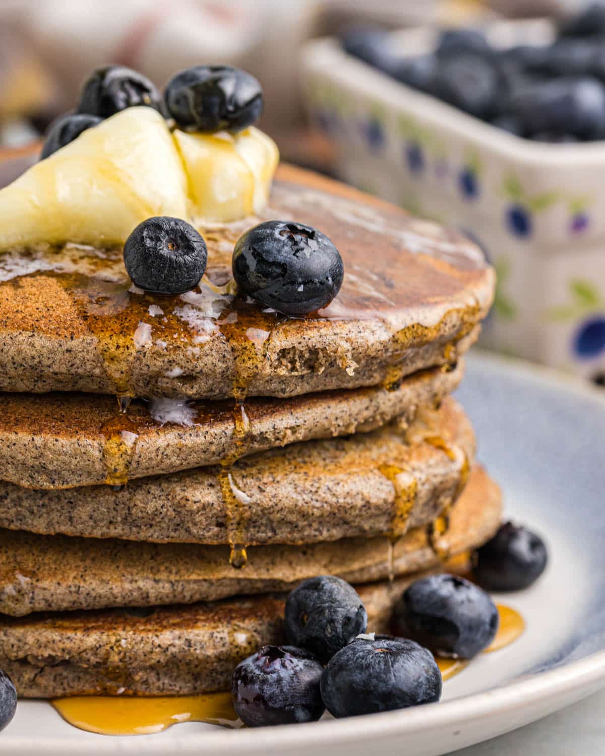 a stack of buckwheat pancakes with syrup and blueberries