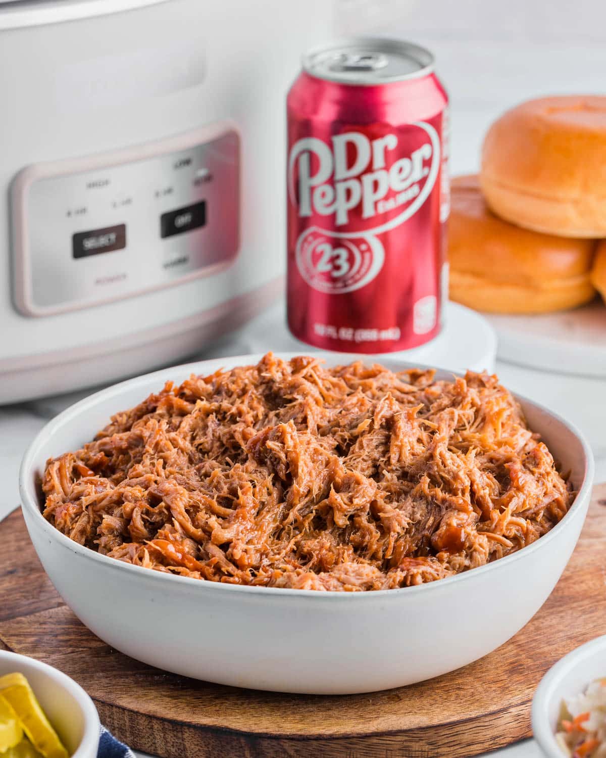 a bowl of pulled pork with dr pepper and a slow cooker in the background