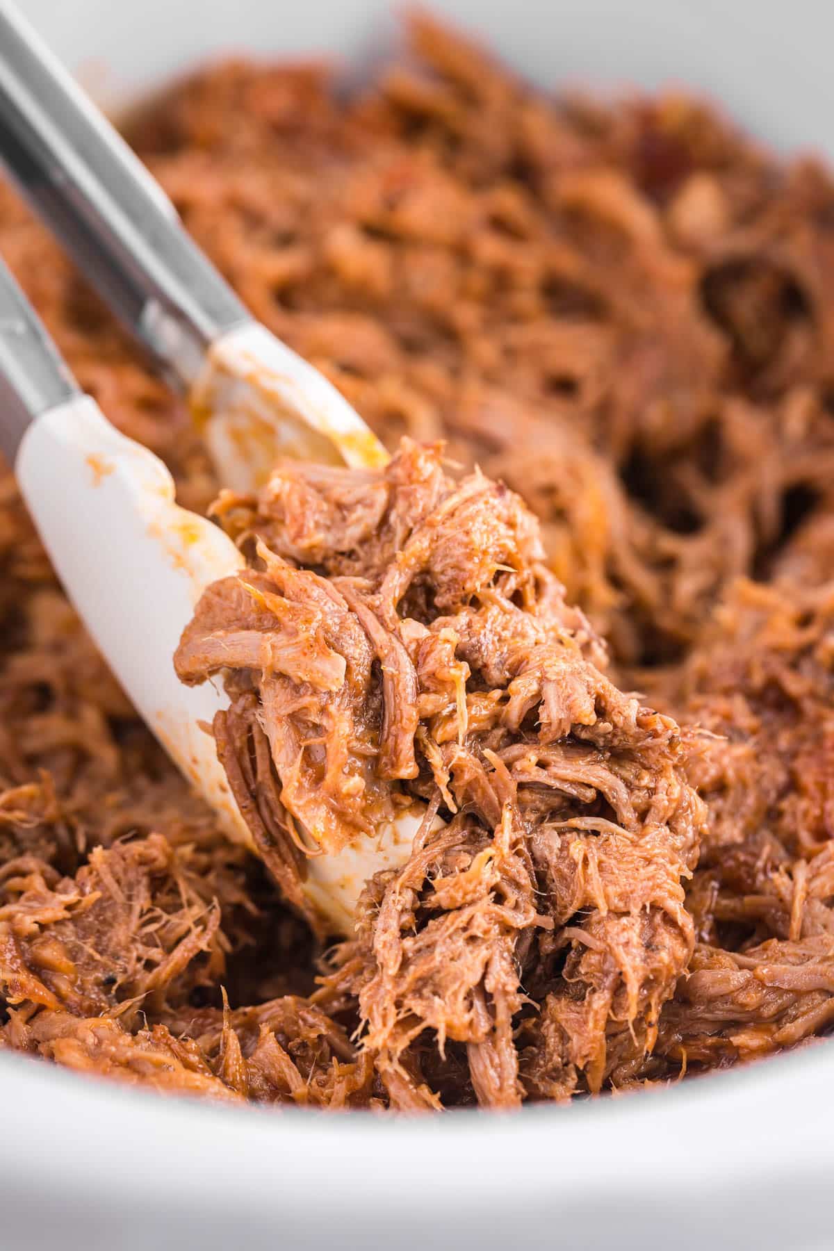 tongs holding pulled pork in a bowl