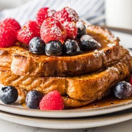 three pieces of french toast on a plate with fresh fruit and syrup