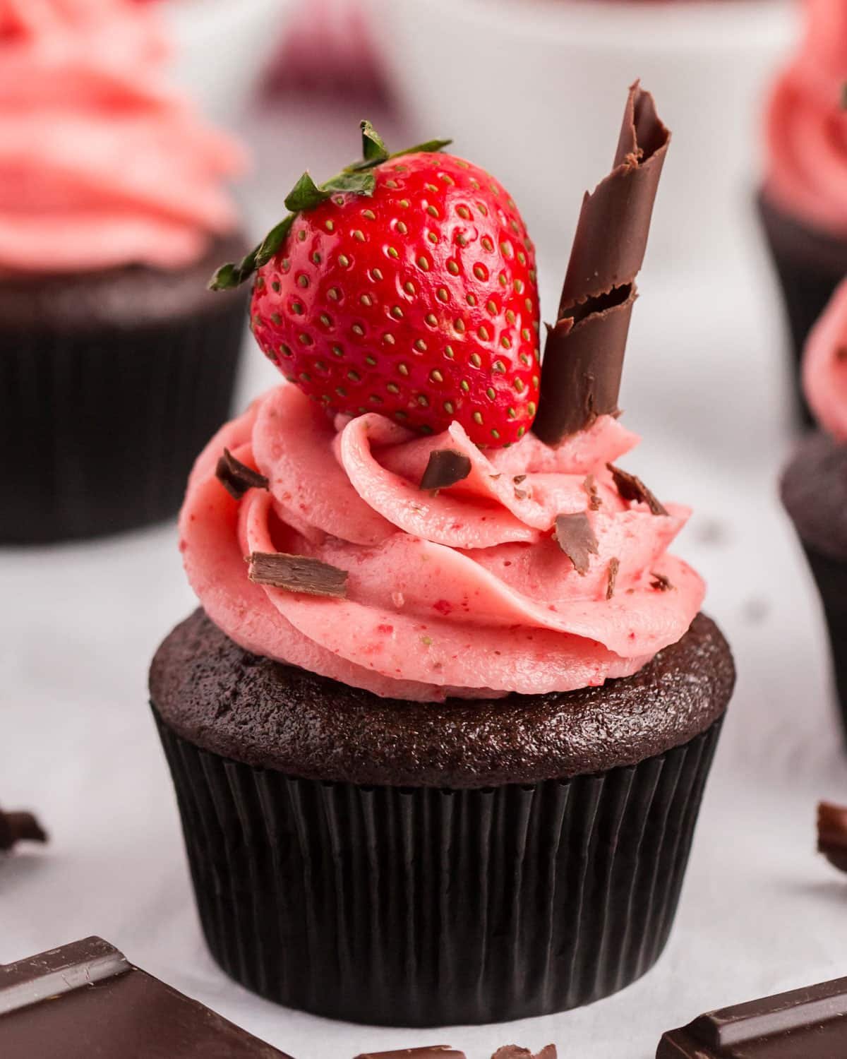 a chocolate cupcake with strawberry frosting and a strawberry sitting on top