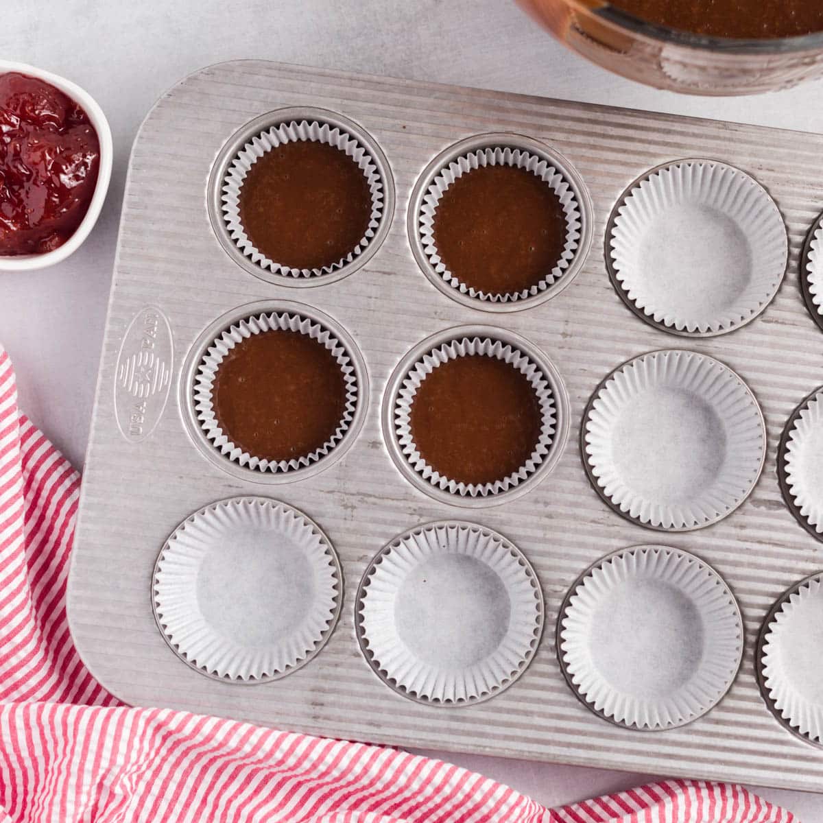 a muffin pan with muffin liners, 4 filled with chocolate cake batter