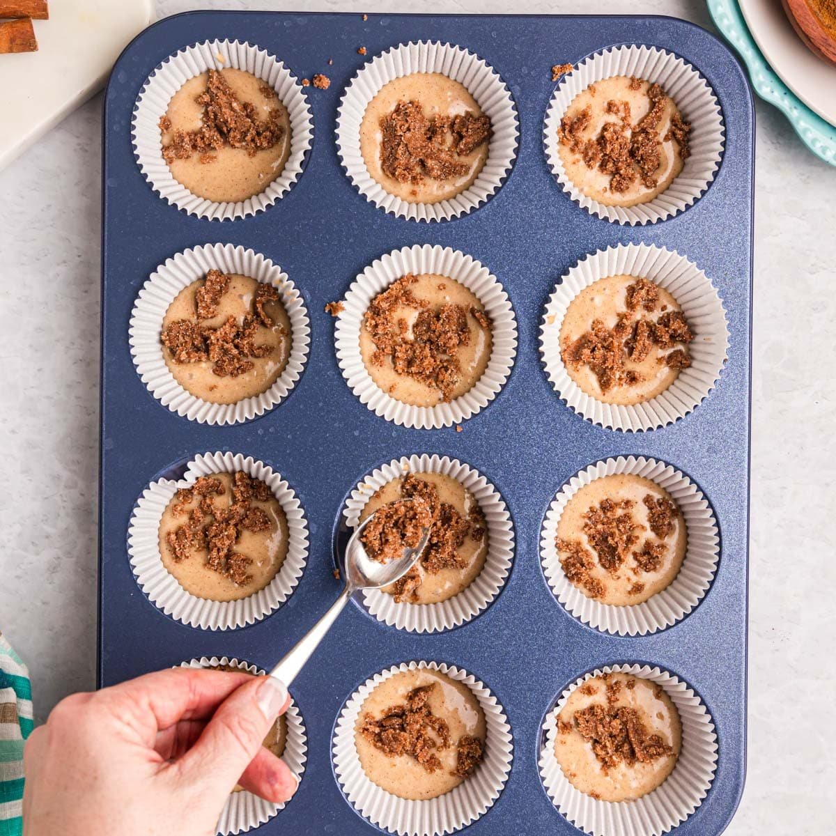 spooning cinnamon sugar streusel over muffin batter