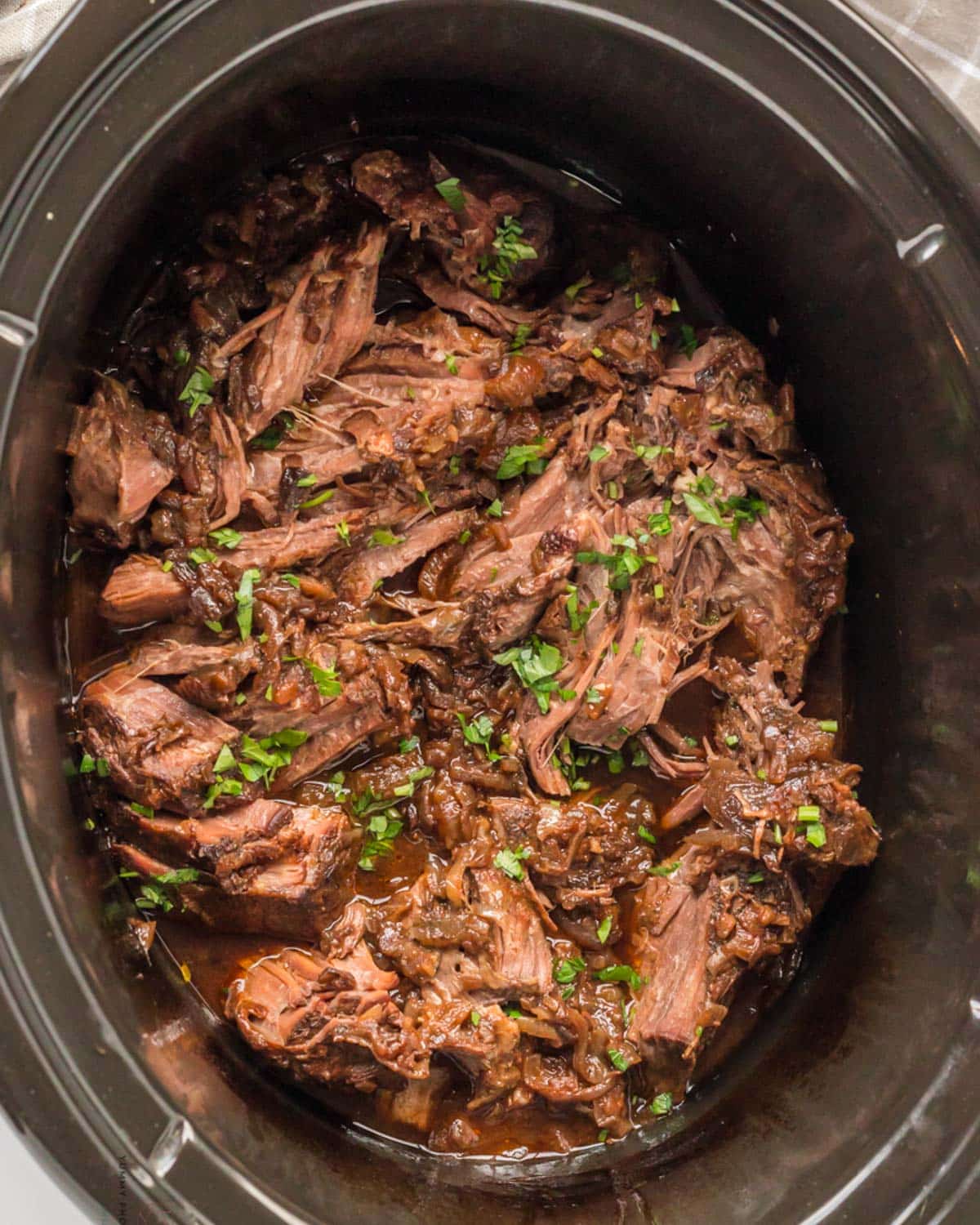 french onion pot roast cooked in a slow cooker with fresh parsley on top