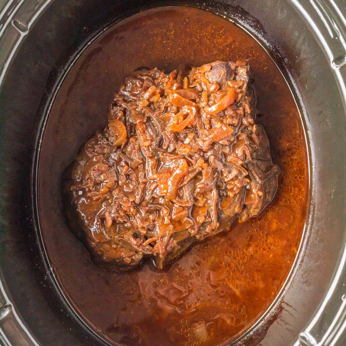 cooked pot roast with onions on top in a slow cooker