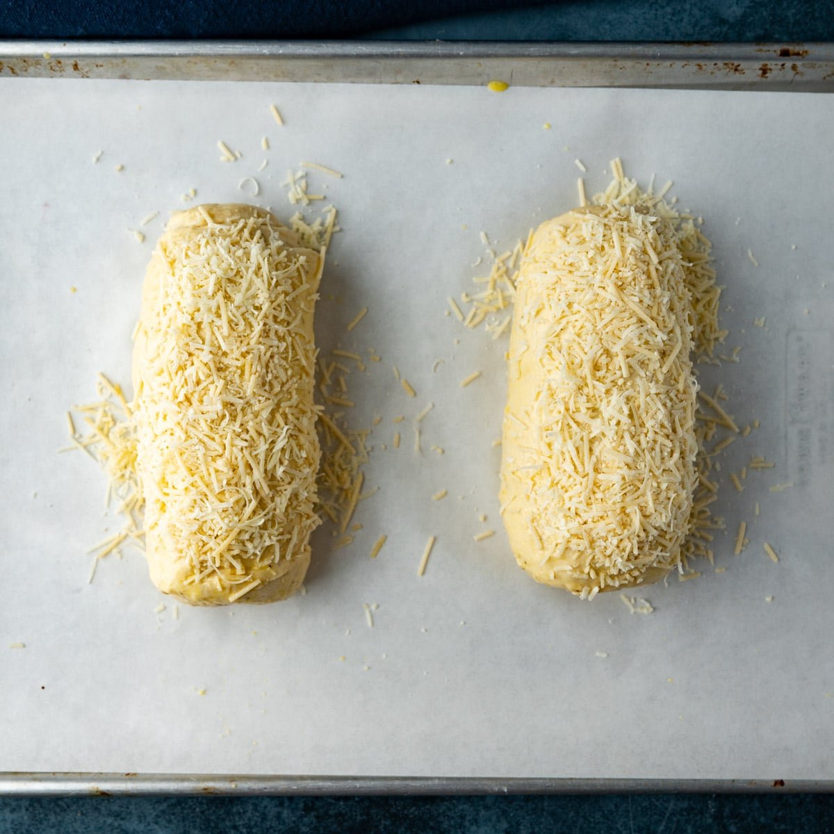 two loaves of unbaked bread dough with asiago cheese on top