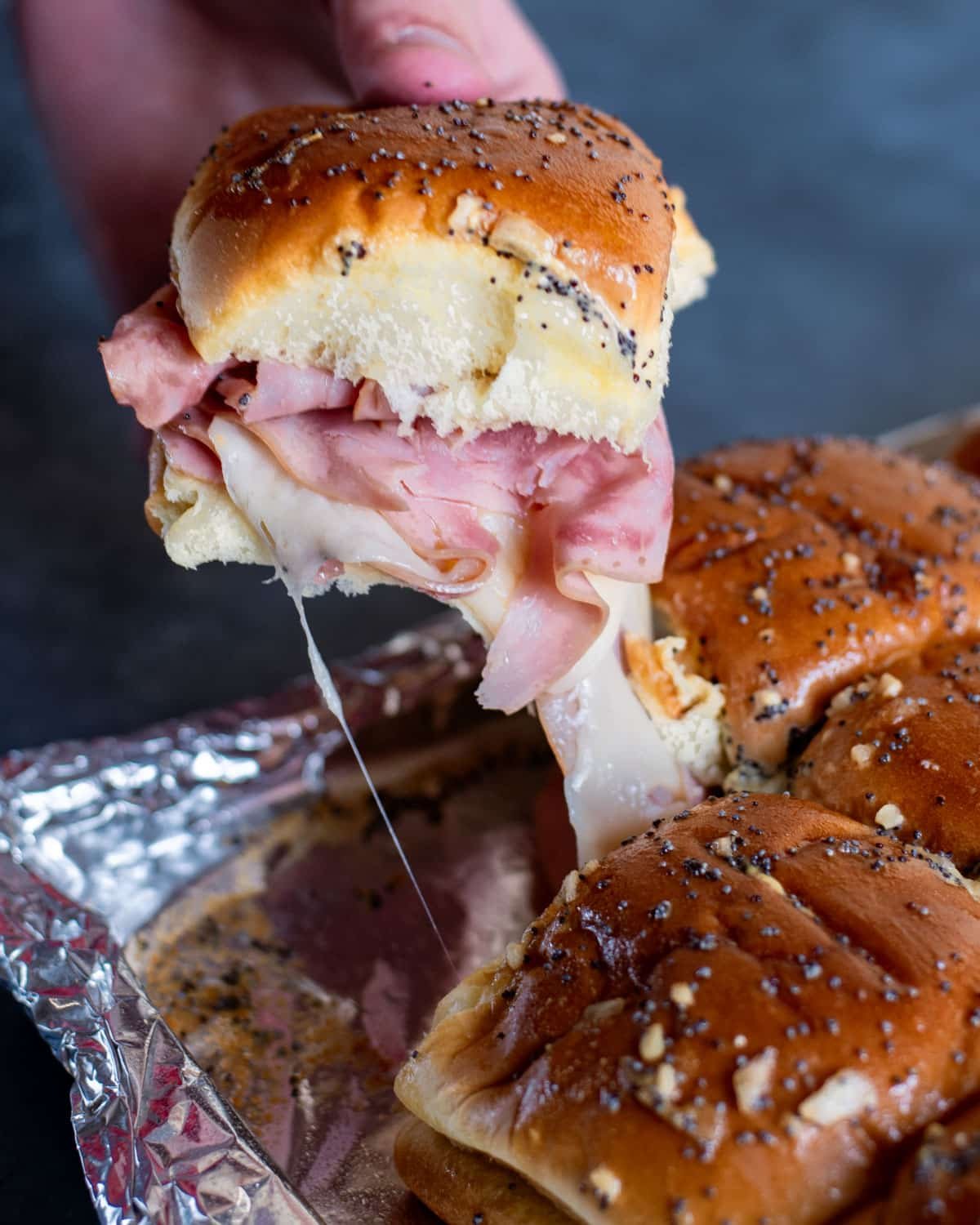 a hand pulling a ham sandwich with melty cheese