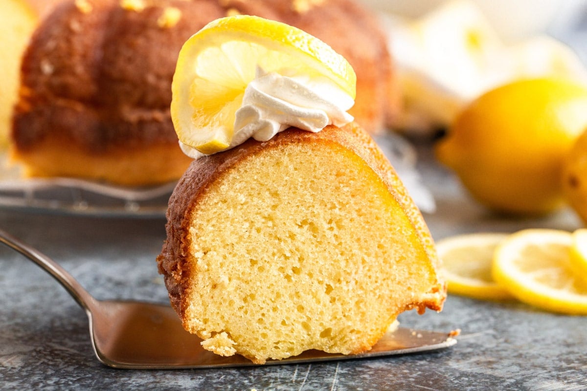 a slice of lemon pound cake on a spatula with whipped cream and a lemon slice