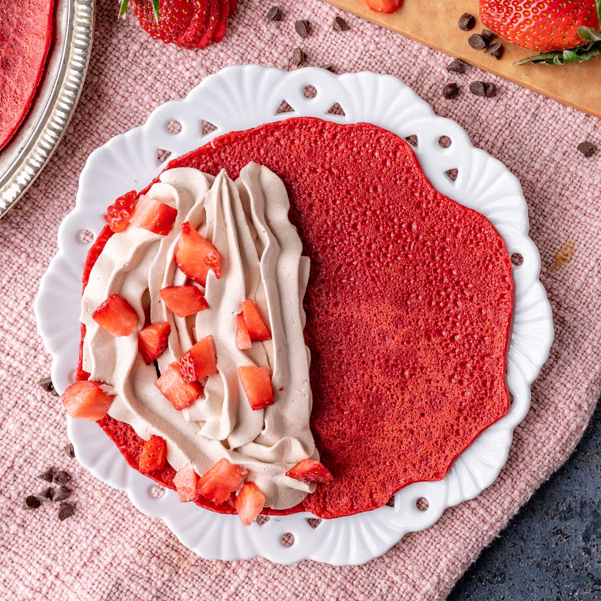 a red velvet crepe, half covered with whipped cream and strawberries