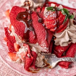 a plate of red velvet crepes with one bite on a fork