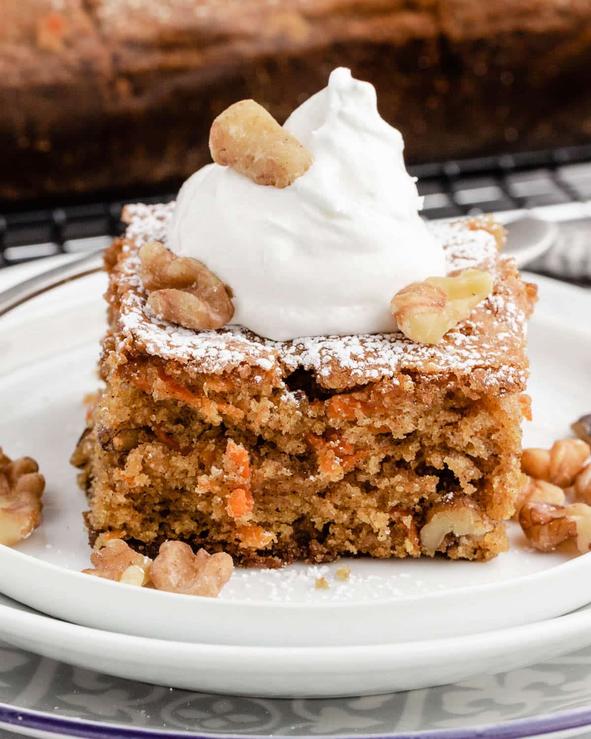 a piece of carrot cake sitting on a plate with whipped cream and walnuts