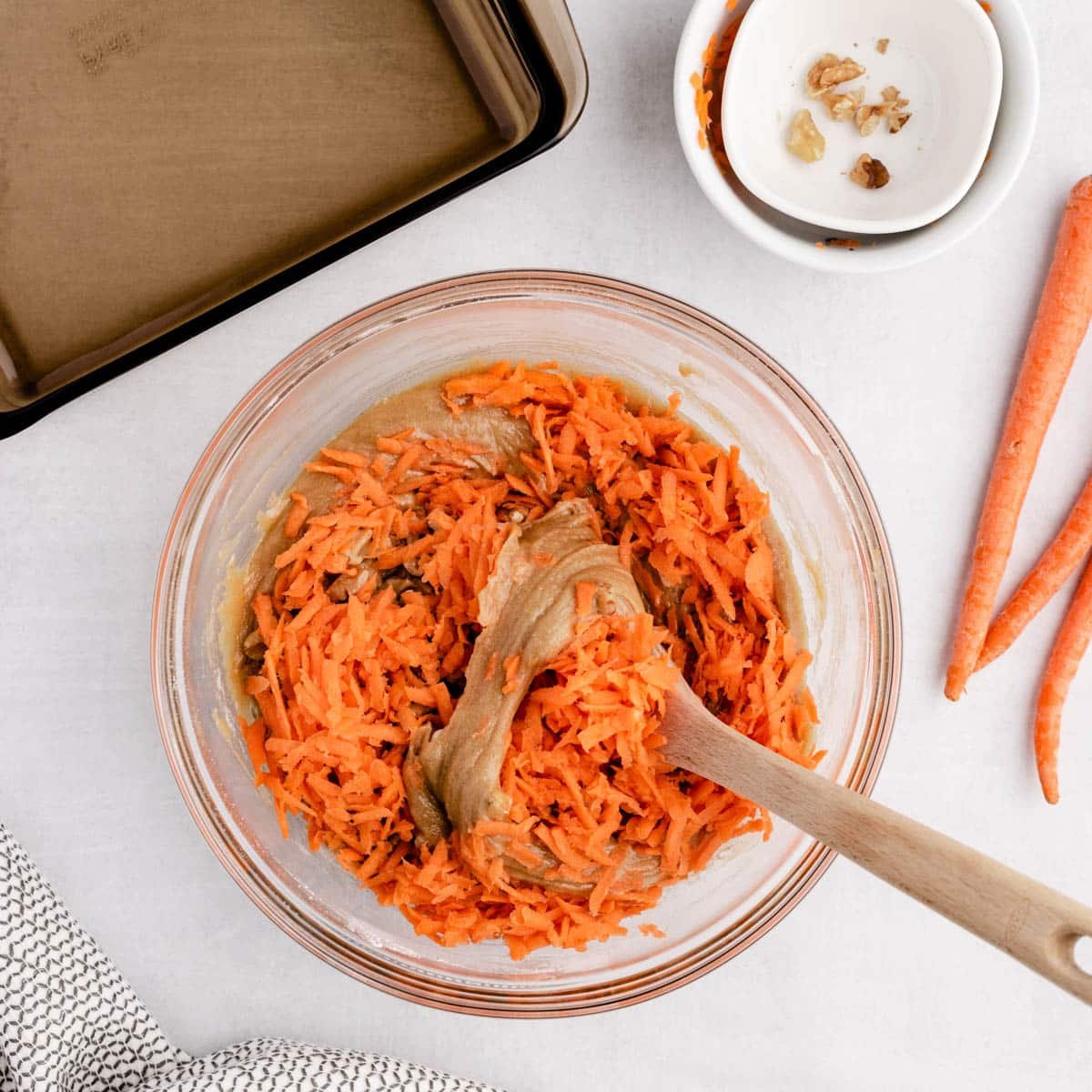 folding shredded carrots into a mixing bowl with cake batter