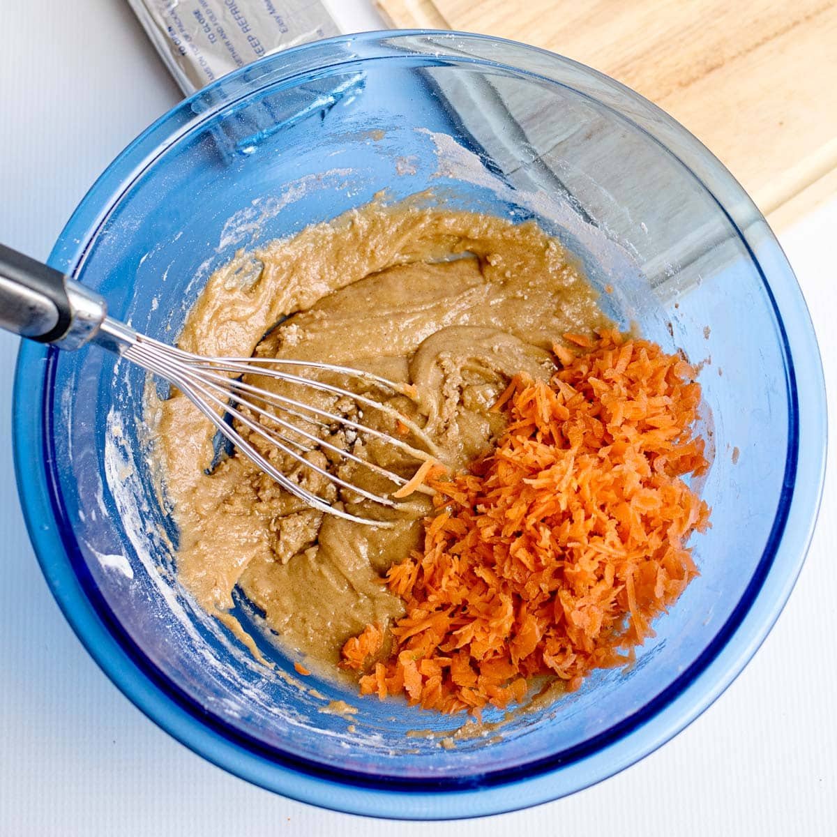 grated carrots over carrot cake batter in a bowl