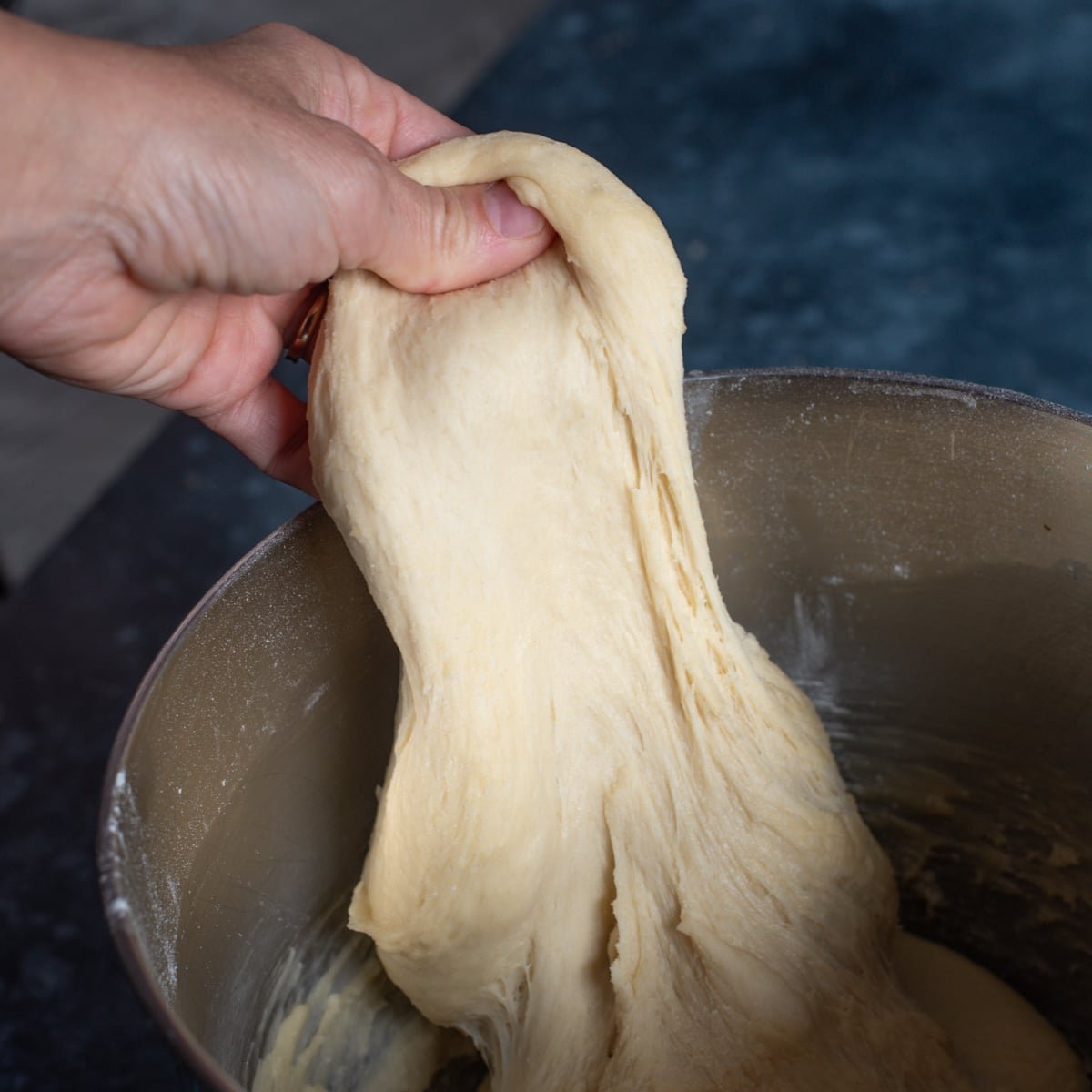 a hand pulling bread dough up from a bowl