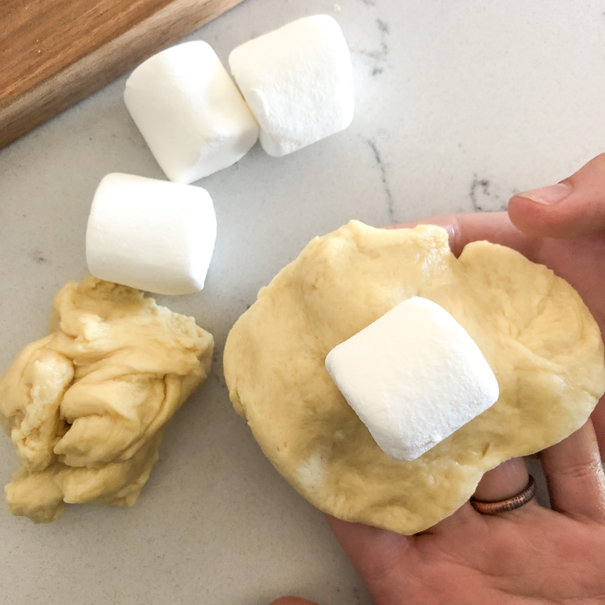 a hand holding bread dough with a marshmallow sitting on top