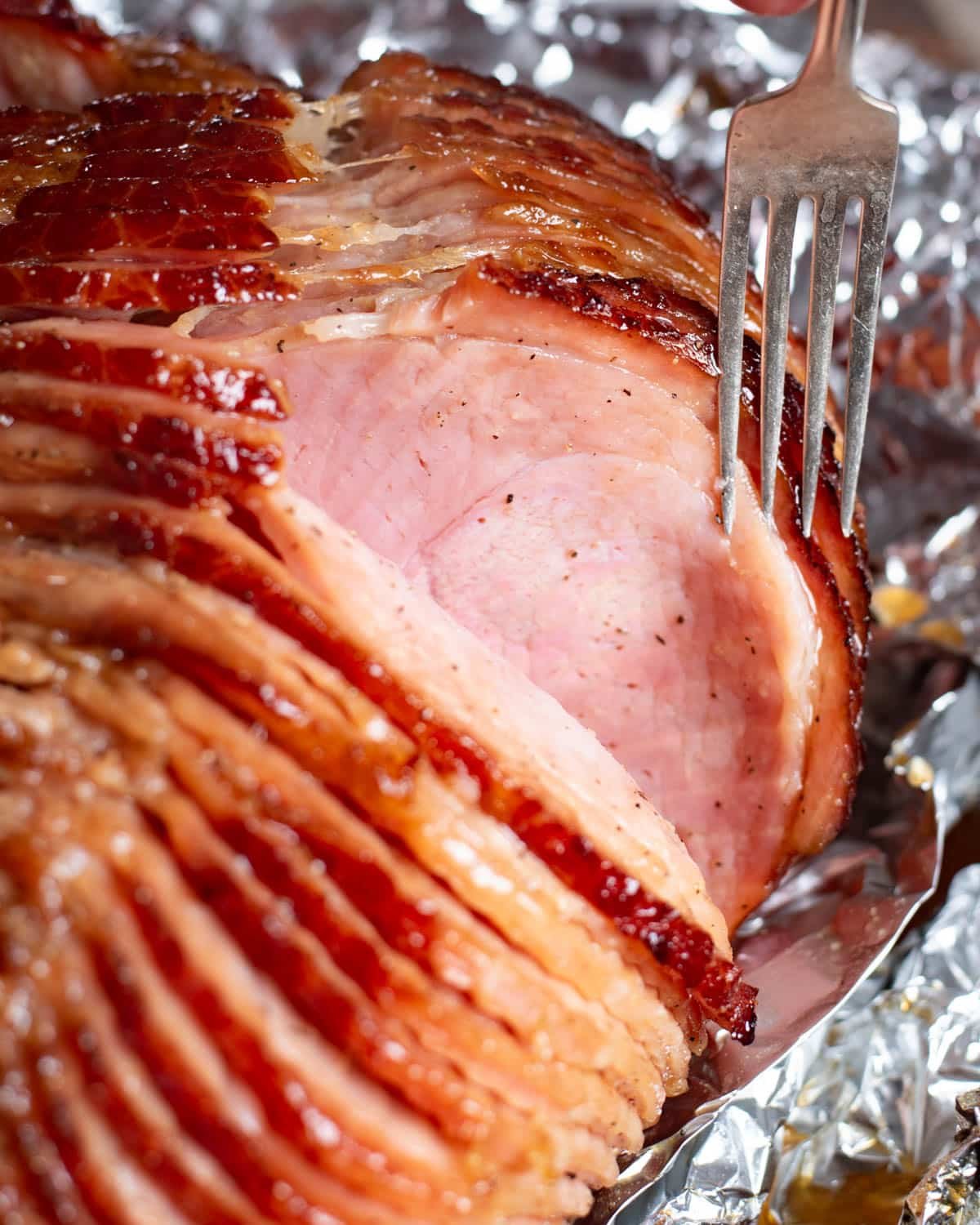 a fork pulling back slices of a honey glazed ham