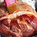 a pastry brush brushing honey glaze over a sliced ham