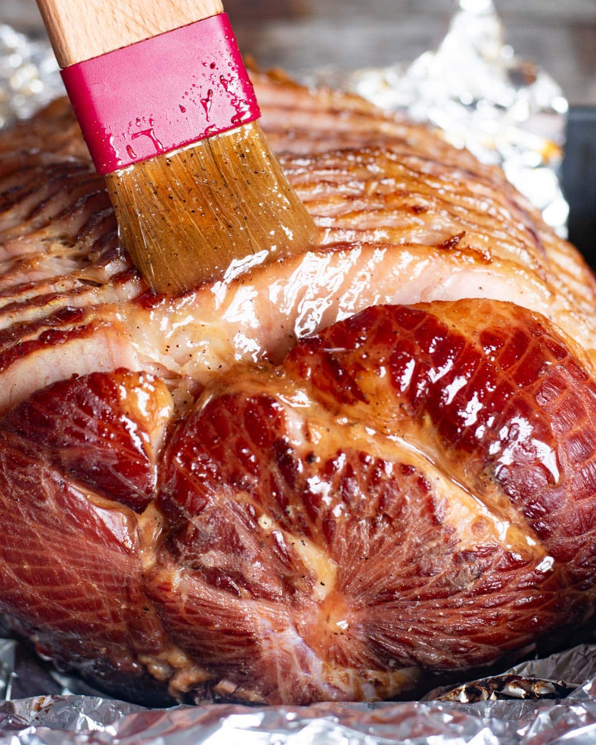 a pastry brush brushing honey glaze over a sliced ham