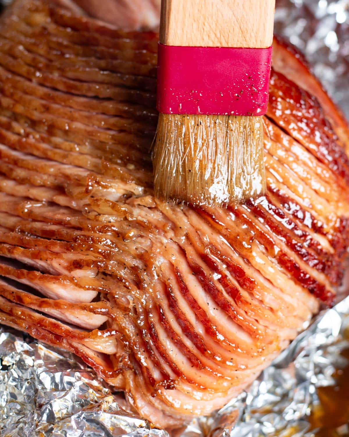 a brush brushing sweet glaze over a sliced ham