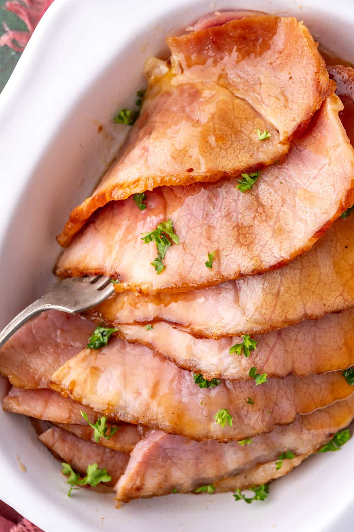 overhead view of sliced ham in a white dish with a fork