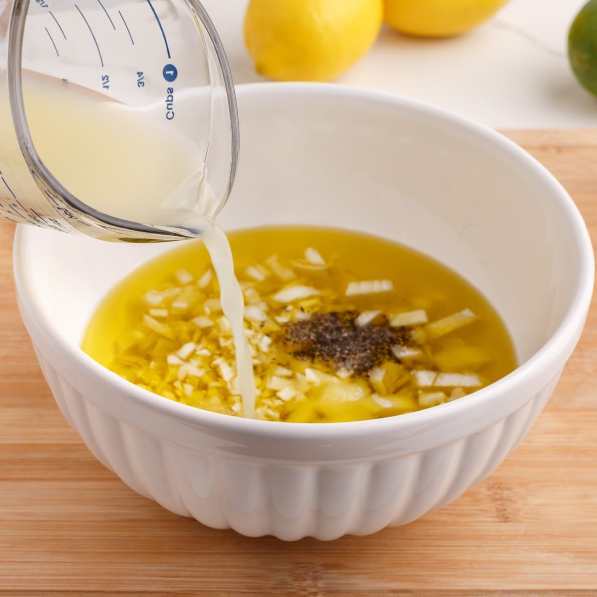lemon juice pouring into a bowl with oil and onion