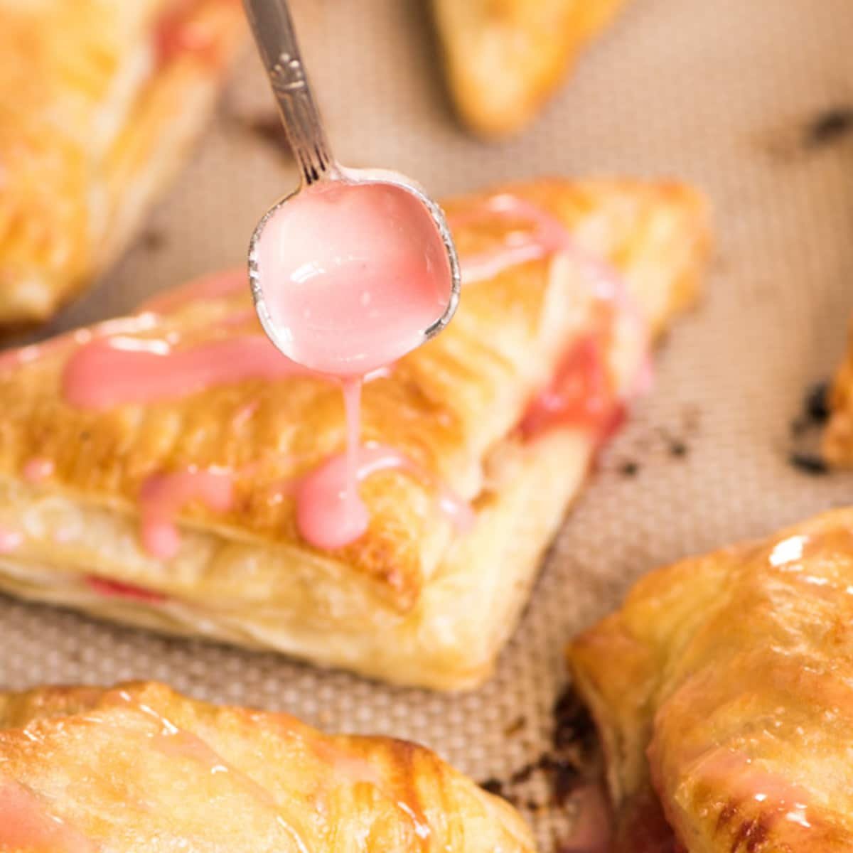 spooning strawberry glaze over puff pastry turnovers