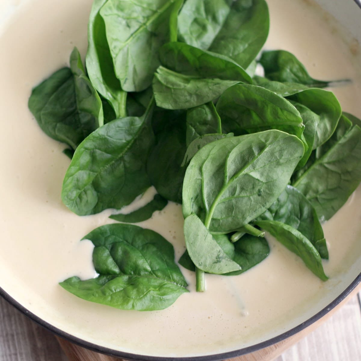 fresh spinach over alfredo sauce in a skillet