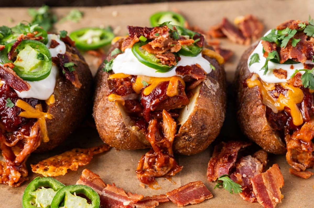 3 loaded baked potatoes with pulled pork on a table