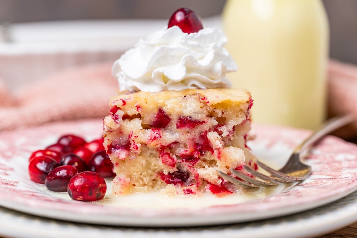 a piece of white cake with cranberries and whipped cream on top