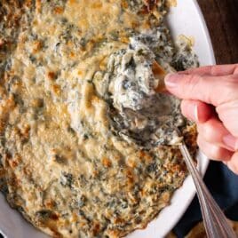 a hand dipping a chip into spinach artichoke dip