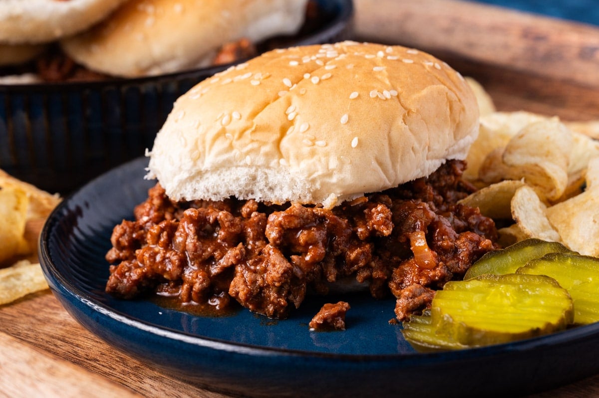 a sloppy joe sandwich on a plate with pickles and chips